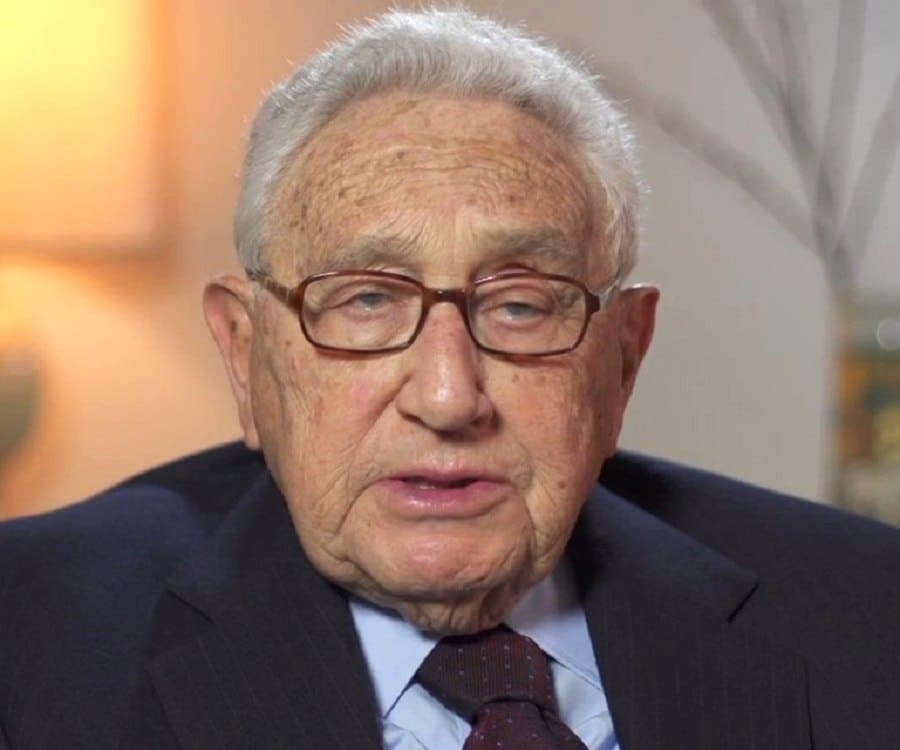 A man in suit and glasses sitting down.