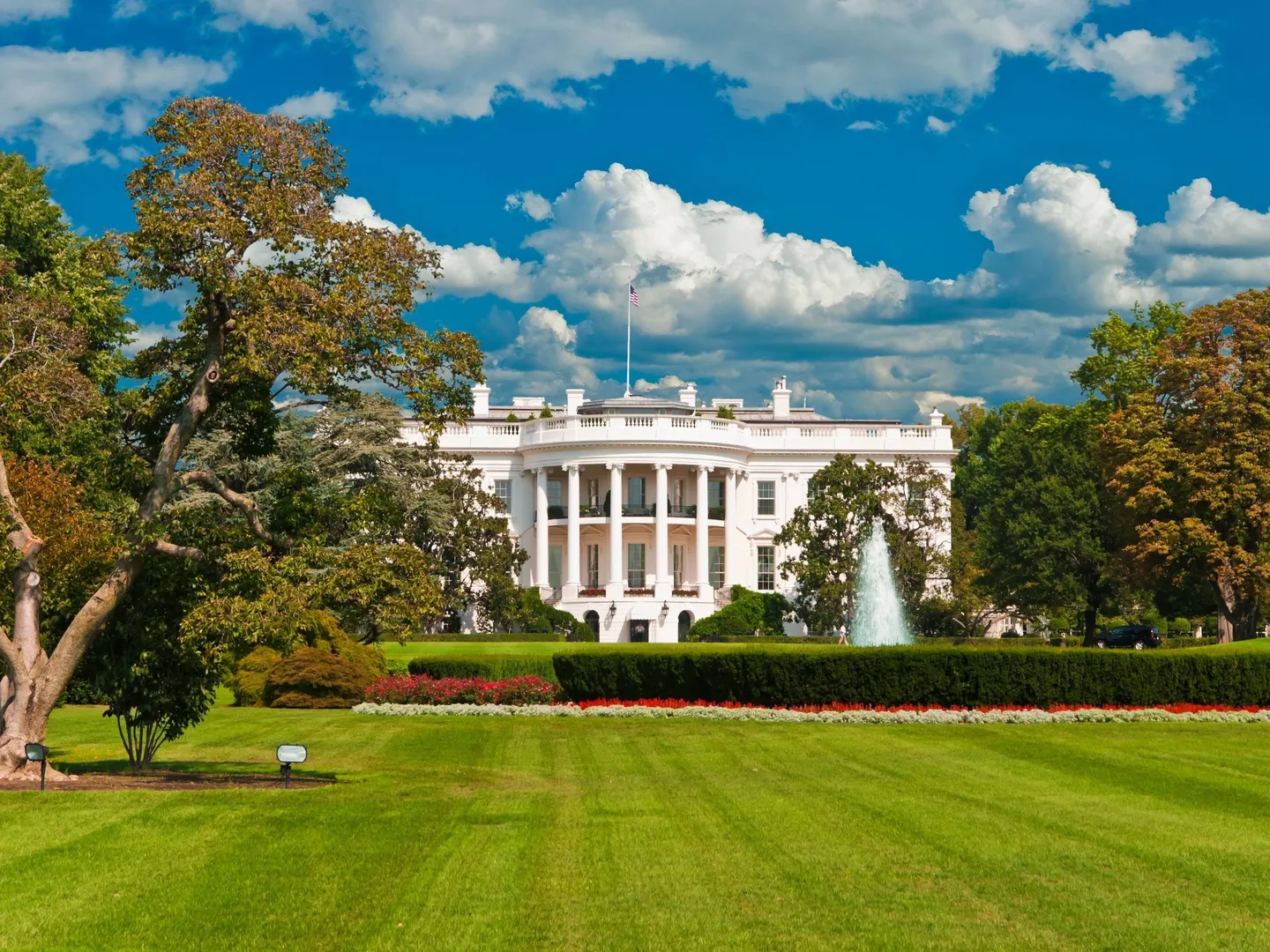 A white house with trees and bushes in front of it.