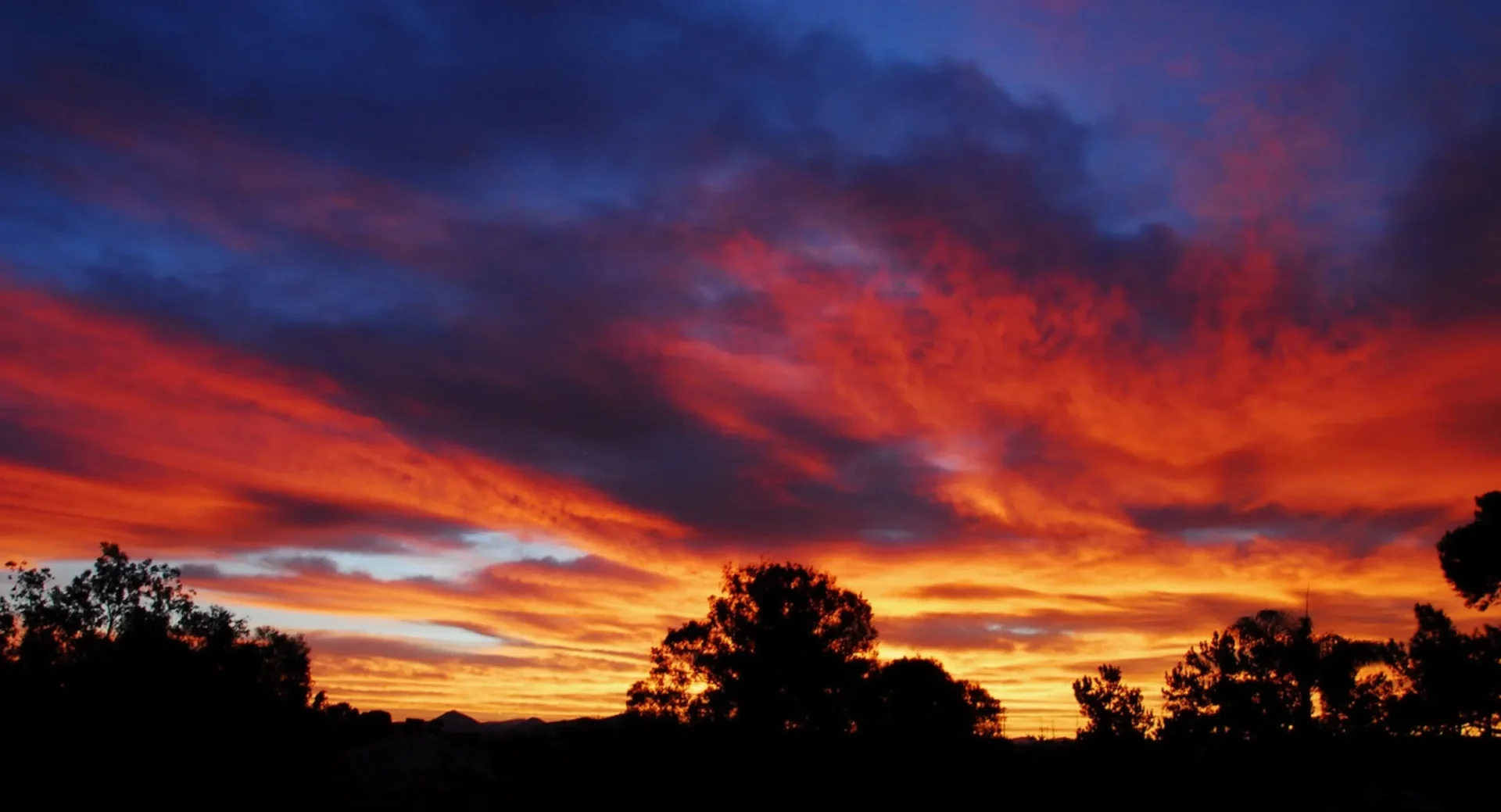 A sunset with clouds in the sky and trees.